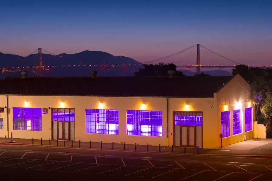 Di notte l'edificio di Fort Mason è illuminato da una luce viola interna, con il ponte sullo sfondo.